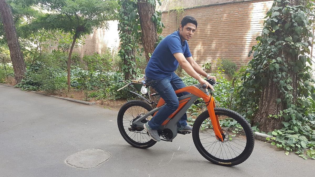 Mand kører på en orange elcykel ad en sti mellem grønne træer