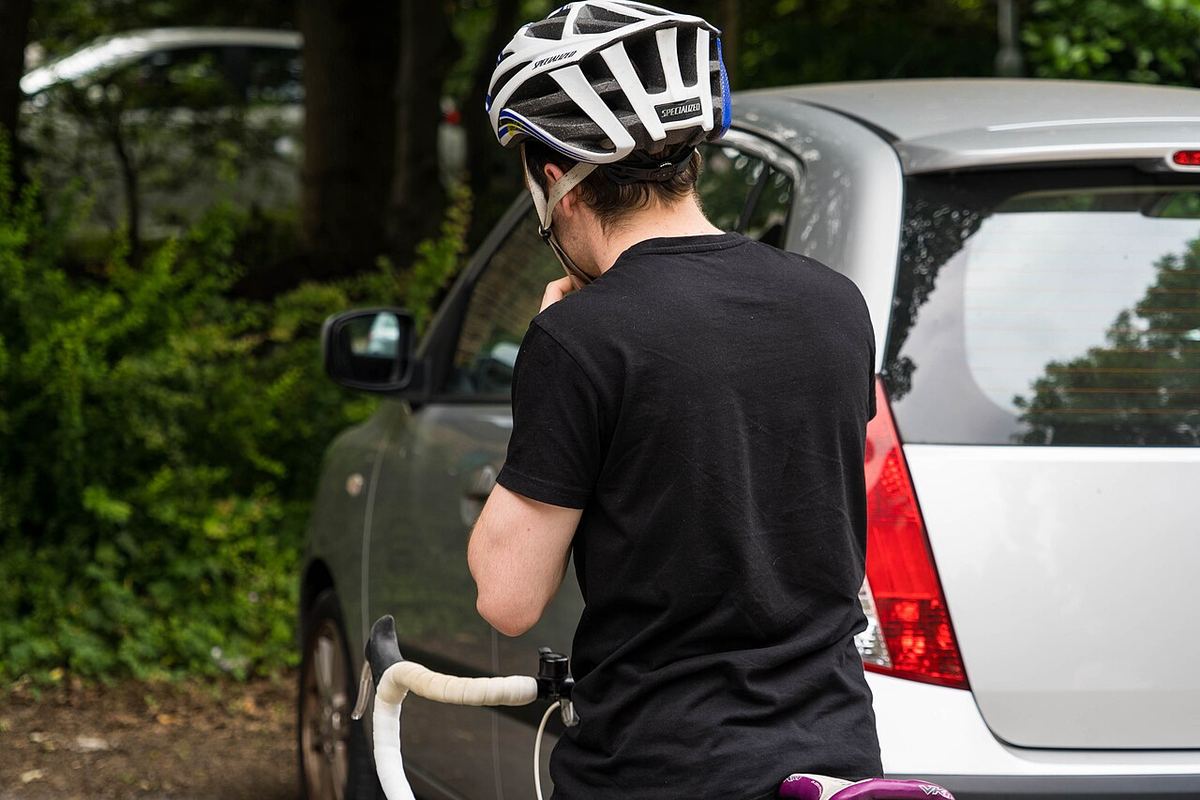 Cyklist tager cykelhjelm på ved siden af en parkeret bil