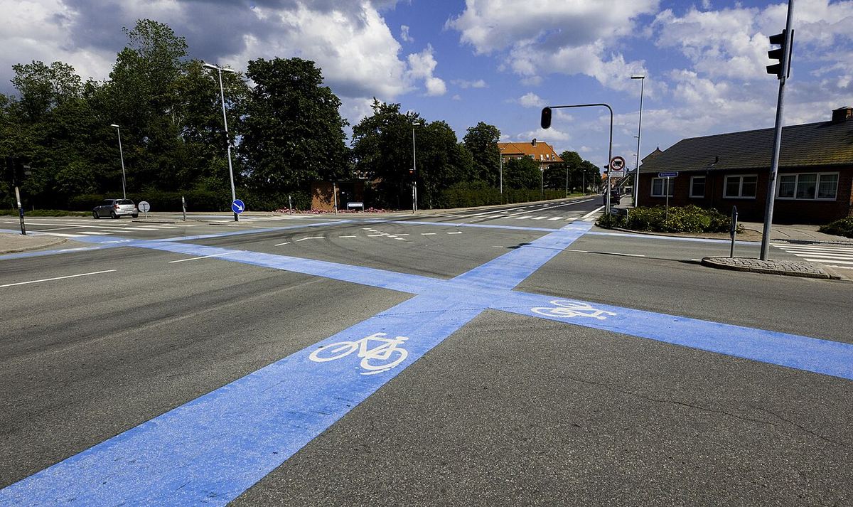Blå cykelfelter med hvide cykelsymboler krydser et stort vejkryds i Danmark