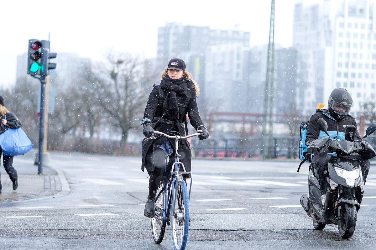 Kvinde cykler gennem et vejkryds i let snevejr i København